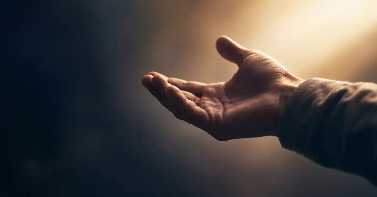 A human hand extended palm up, reaching from soft darkness into warm light — representing an offer of connection.